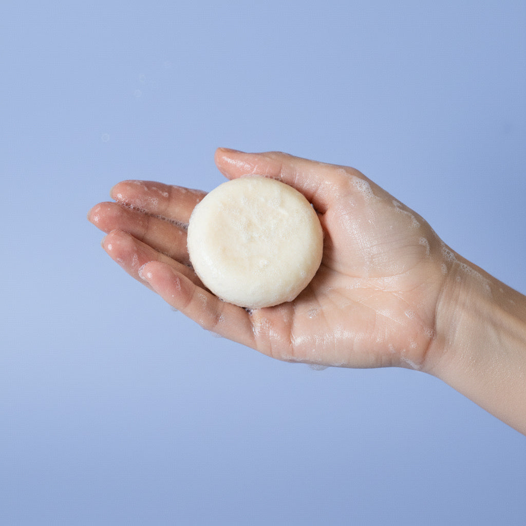 Hand holding a round, white bar of soap against a light blue background
